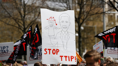 Pancarta con un dibujo de Obama, mientras sujeta a Merkel representada como una marioneta. REUTERS/Kai Pfaffenbach