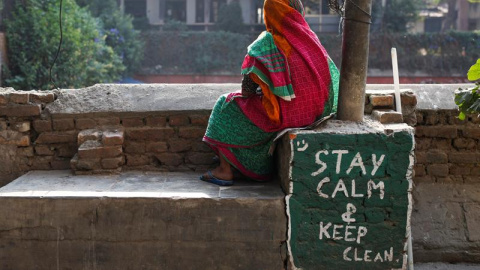 Una mujer nepalesa descansa sentada junto a una pintada con el mensaje "Permanece tranquilo y limpio" mientras siguen las obras de reconstrucción de un grifo de agua potable comunitario que resultó dañado en el terremoto, en Katmandú, Nepal