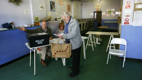 Un hombre recoge su papeleta de voto de las manos de secretarios de colegio en una lavandería pública, que se utiliza como un centro de votación en Oxford./ REUTERS / Eddie Keogh