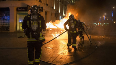 Bomberos tratan de apagar las llamas de un coche de Policía incendiado. - AFP