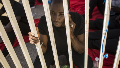 Un joven de senegal llama por teléfono en el muelle del puerto de Algeciras, donde ha pasado dos noches por falta de espacio en dependencias policiales y polideportivos. JAIRO VARGAS