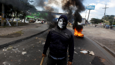Un manifestante enmascarado mira a la cámara mientras unos neumáticos arden al fondo. REUTERS/Jorge Cabrera Un manifestante enmascarado mira a la cámara mientras unos neumáticos arden al fondo. REUTERS/Jorge Cabrera