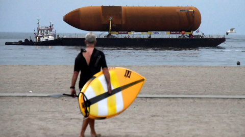 Un deportista de paddle board camina hacia el agua mientras que contempla un transbordador espacial que es transportado por medio de barcazas para su eventual colocación en el Centro de Ciencias de California en Marina del Rey, California. 