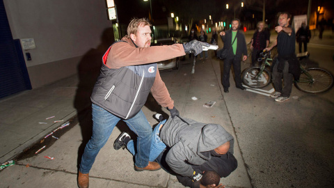 Un oficial de policía de paisano apunta contra su arma contra los manifestantes en Oakland (California) tras ser atacados por algunos de los congregados. Protestan por la decisión de la justicia de exonerar a Darren Wilson, un policía blanc