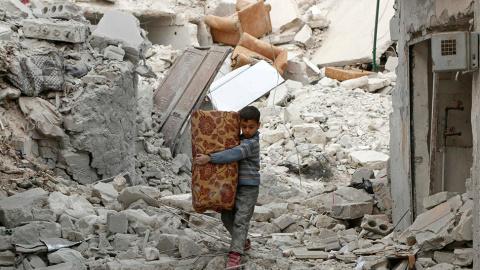 Un niño lleva sus pertenencias mientras camina sobre los escombros en el barrio de al-Kalaseh, de Alepo. // HOSAM KATAN (REUTERS)