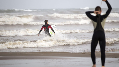 Dos jóvenes surfistas se disponen, esta tarde, a entrar en el mar a disfrutar de las olas que el temporal de Levante lleva hasta la orilla de la playa de Las Arenas de Valencia. El temporal de lluvias que afecta a la Comunitat Valenciana ha