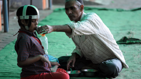 Un hombre da de comer a un niño, víctima de segunda generación de la catástrofe de Bhopal. // AFP