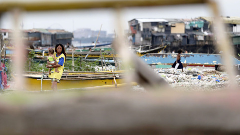 Una madre y su hijo caminan junto a varias barcas de pesca castigadas por el paso del tifón Hagupit. // EFE/EPA/DENNIS M. SABANGAN