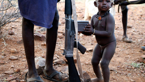 Un niño de Turkana se aferra a la escopeta de su padre, en un pueblo al noroeste de Kenia. /GORAN TOMASEVIC (REUTERS