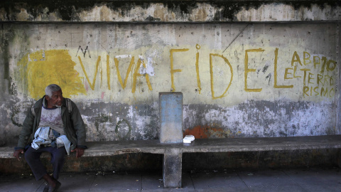 Un hombre sentado en un banco junto a una pintada que reza "Larga vida a Fidel". REUTERS/Stringer