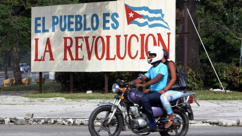 Dos personas pasan en una moto delante de un cartel alusivo a la revolución cubana, en La Habana. EFE/Ernesto Mastrascusa