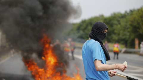 Un manifestante enmascarado junto a neumáticos en llamas que bloquean la carretera durante las protestas contra la ley la reforma laboral en Nantes, Francia. REUTERS/Stephane Mahe