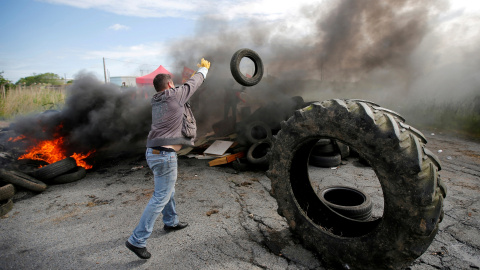 Un manifestante empleado de una petrolera lanza de un neumático sobre una barricada en llamas para bloquear la entrada del depósito.- REUTERS / Stephane Mahe / Foto