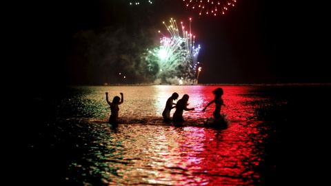 Cuatro mujeres se bañan en el agua mientras a lo lejos, en la Playa de la Misericordia de Málaga, se ven fuegos artificiales para celebrar San Juan./ REUTERS/ Jon Nazca
