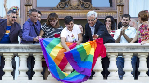 El alcalde de Valencia, Joan Ribó (centro), despliega desde el balcón del Ayuntamiento la bandera arco iris con motivo del Día Internacional del colectivo LGTB. /EFE El alcalde de Valencia, Joan Ribó (centro), despliega desde el balcón del Ayuntamiento la bandera arco iris con motivo del Día Internacional del colectivo LGTB. /EFE