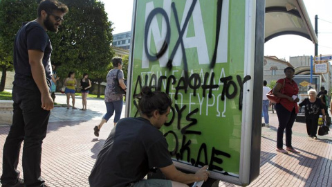 Un joven escribe con grafiti "No" sobre un cartel que pide el "Sí" en el referendum del domingo en una marquesina de autobús en Atenas. - EFE