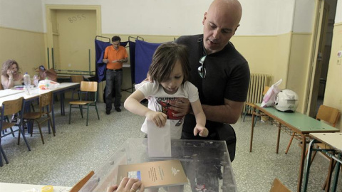 Una niña ayuda a su padre a introducir su voto en la urna en un colegio electoral de Atenas. EFE/EPA/Orestis Panagiotou