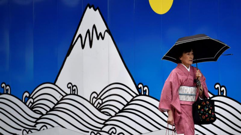 Una mujer vestida con un kimono pasa delante de un andamio decorado con el dibujo de una montaña en el distrito comercial de Ginza en Tokio, Japón. EFE/Franck Robichon