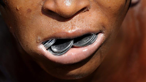 Un niño indio sostiene en el interior de la boca las monedas que ha recuperado del fondo del contaminado río Adi Ganga, en las proximidades del templo Kalighat en Calcuta, al este de la India. EFE/Piyal Adhikary