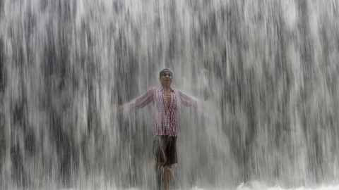 Un niño bajo el agua emanada de una presa  a lo largo del lago Powai tras fuertes lluvias en Mumbai , India.- REUTERS / Shailesh Andrad