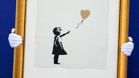 Un empleado de la casa de subastas Christie's sostiene una versión de la obra 'Niña con globo', de Banksy. / EFE