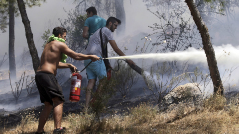 Varios voluntarios intentan extinguir las llamas en el suburbio de Karea en Atenas (Grecia) hoy. Un gran incendio originado esta madrugada en la región griega de Laconia, en el sur del Peloponeso, ha obligado a evacuar tres pueblos y dos ca