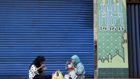 Dos mujeres almuerzan frente a un local que permanece cerrado con motivo de la festividad del Eid al-Fitr, en Yakarta (Indonesia) hoy, 21 de julio de 2015. El Banco Central Indonesio informó que la proyección de inflación en julio es de un 