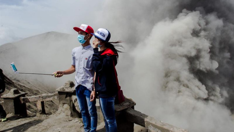 Dos jóvenes posan para un selfie mientras el volcán Bromo arroja cenizas al aire durante una erupción volcánica en Probolinggo, Indonesia. EFE/Fully Handoko