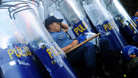 Un policía se apoya en escudos antidisturbios antes de su despliegue para bloquear los manifestantes que marchan hacia el parlamento en los suburbios de Manila, horas antes de que el presidente Benigno Aquino pronuncie su discurso anual. AF