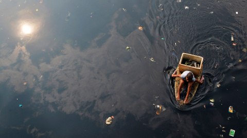 Una mujer rema con las manos en un bote improvisado mientras recoge basura en un río contaminado en la ciudad de Navotas (Filipinas).- ESDRAS ACAYAN (REUTERS)