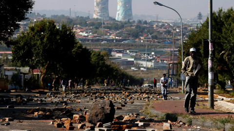 Un hombre camina por una calle llena de rocas y piedras, resultado del enfrentamiento entre manifestantes y policía en Soweto (Suráfrica) por los altos precios de la electricidad.- SIPHIWE SIBEKO (REUTERS)