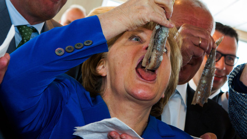 La canciller alemana Angela Merkel se come un arenque en Sassnitz, Alemania del este.- JENS BATTNER (AFP)