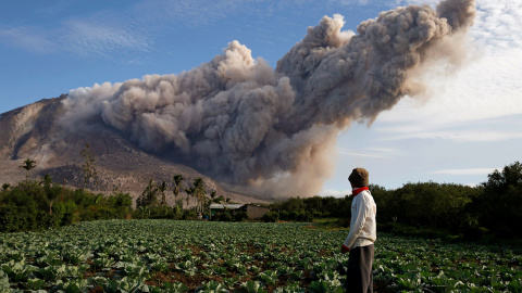 Un residente en su huerta mientras al fondo el volcán Monte Sinabung arroja cenizas.- BEAWIHARTA (REUTERS)