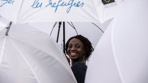 Una mujer sonríe mientras la gente se manifiesta sujetando paraguas blancos, con motivo del Día Mundial del Refugiado en Lyon- JEAN-PHILIPPE KSIAZEK (AFP)