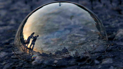La gente, reflejada en una burbuja de jabón en la carretera, durante la noche e Nueva Delhi.- ANINDITO NUKHERJEE (REUTERS)