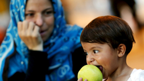 Un niño, hijo de inmigrantes llegados a Hungría, se come una manzana ante los ojos de su madre en la estación de tren de Budapest. REUTERS/Laszlo Balogh