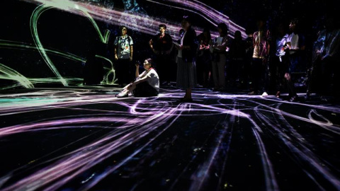 Varios visitantes observan la obra de arte "Crows are Chased and the Chasing Crows are Destined to be Chased as well, Blossoming on Collision - Light in Space" (lit. "Los Cuervos son Perseguidos y los Cuervos Perseguidores están Destinados 