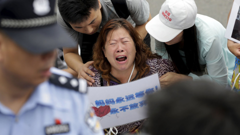Una mujer cuyo familiar estaba a bordo del vuelo MH370 de Malaysia Airlines, sostiene un cartel que dice : "Mamá estará siempre aquí esperando por ti, nunca te rindas", mientras llora y se arrodilla junto con miembros de la familia ante los