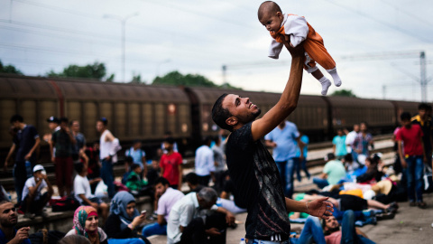 Un inmigrante levanta su bebé mientras espera un tren en dirección a la frontera con Serbia, en la estación de tren en Gevgelija, en la frontera de Macedonia y Grecia el 6 de agosto de 2015.- AFP PHOTO / DIMITAR DILKOFF