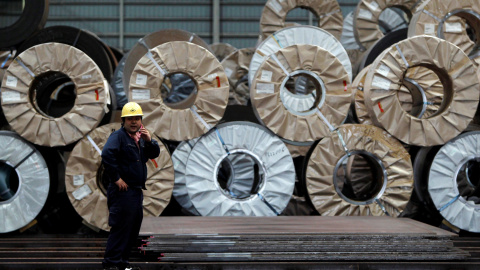 Un trabajador utiliza un teléfono móvil delante de bobinas y chapas de acero en un almacén de distribución en Urayasu. REUTERS/Toru Hanai
