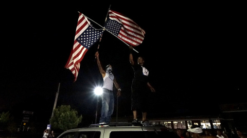 Un manifestante sostiene banderas de Estados Unidos al revés en la parte superior de un coche fuera del departamento de policía de Ferguson . REUTERS / Rick Wilking