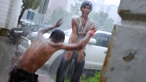 Dos jóvenes indios se divierten jugando bajo un chorro de agua que cae de una fuga en una azotea en el centro de Nueva Delhi, el 11 de agosto de 2015. AFP PHOTO / Roberto SCHMIDT