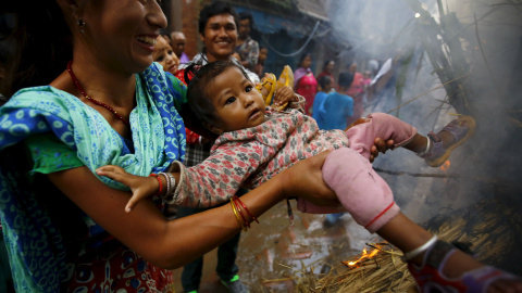 Una mujer pasa a su hijo por encima de la fogata donde fue quemada una efigie del demonio Ghantakarna para simbolizar la destrucción del mal, durante el festival Ghantakarna en la antigua ciudad de Bhaktapur, Nepal 12 de agosto de 2015. REU