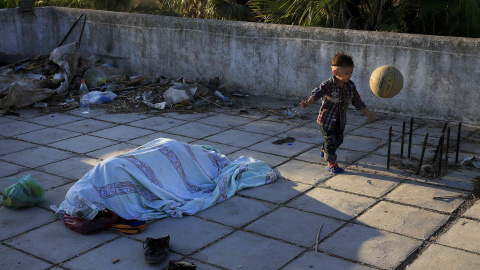 Un niño Pakistaní juega con una pelota mientras otro emigrante duerme en la terraza de un hotel abandonado en la isla griega de Cos, 13 de agosto de 2015. REUTERS / Alkis Konstantinidis