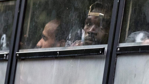 Varios migrantes sudaneses y eritreos miran por las ventanillas de un autobús mientras son desalojados por la policía durante el desmantelamiento de un campamento temporal de inmigrantes principalmente de Sudán y Eritrea, en la avenida Flan