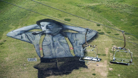 Vista de una imagen que representa a un pastor suizo, hecha con pintura biodegradable, obra del artista francés Saype en 10,000 metros cuadrados de césped en Leysin, Suiza. EFE/Jean-Christophe Bott
