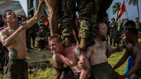 Marines estadounidenses juegan a un juego tradicional indonesio que consiste en escalar un poste resbaladizo para conseguir botellas de Coca-Cola, en la playa Banongan en Situbondo, en el este de la isla de Java.- AFP PHOTO / JUNI KRISWANTO