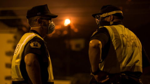 Dos miembros de la policía hacen guardia mientras el fuego se aproxima, en Las Manchas, al suroeste de la isla de La Palma. REUTERS/Borja Suarez