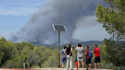 Unos vecinos observan el incendio en La Pobla de Montornès (Tarragona) donde los Bomberos han desalojado hoy la parte alta de la urbanización Castell de Montornès como medida de precaución ante un incendio que arde sin control en una zona f