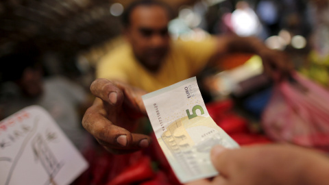 Un vendedor coge un billete de cinco euros de un cliente en el mercado centrasl de Atenas, Grecia. REUTERS/Christian Hartmann